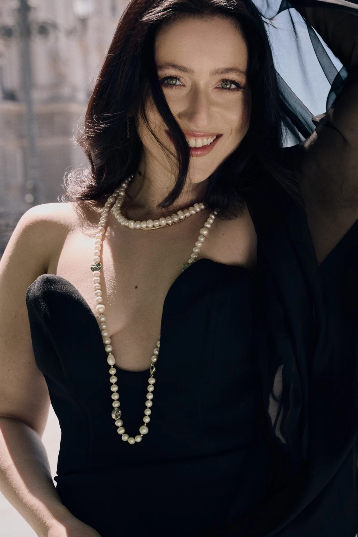 Mané in a black evening dress and pearls, smiling in the sunlight